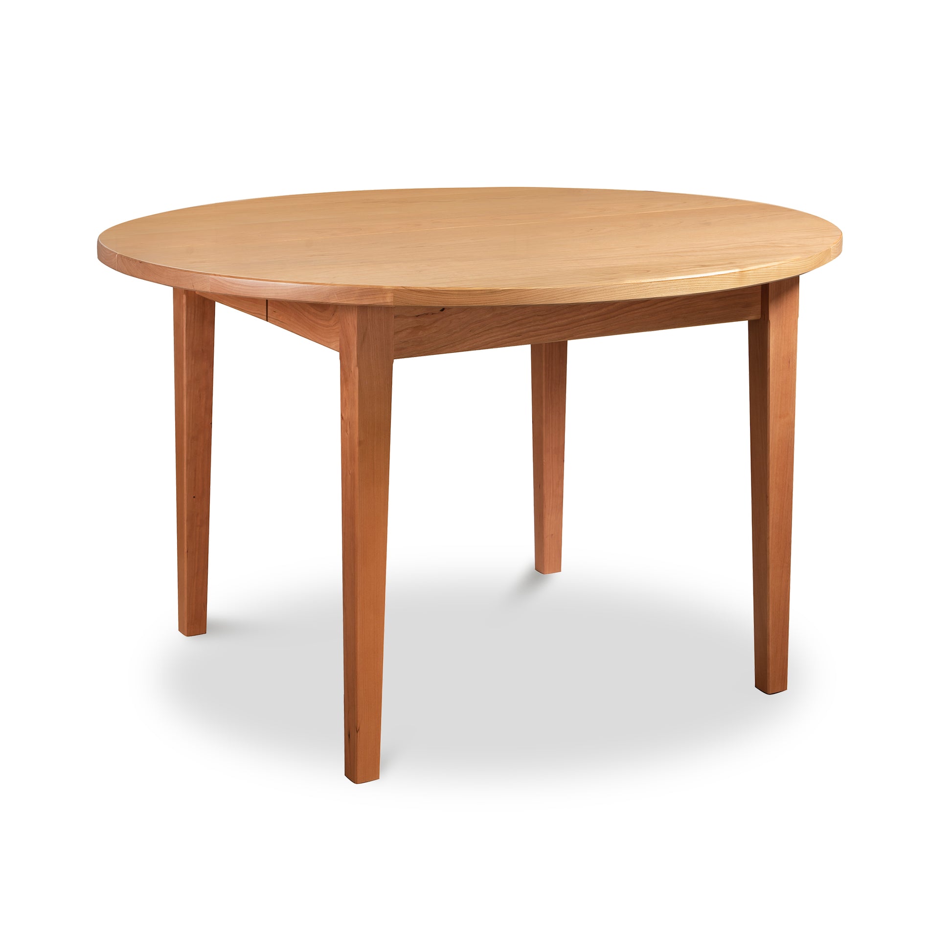 A Vermont Shaker Round Extension Table from Maple Corner Woodworks, with four legs, isolated on a white background. The table has a smooth finish and natural cherry wood texture.
