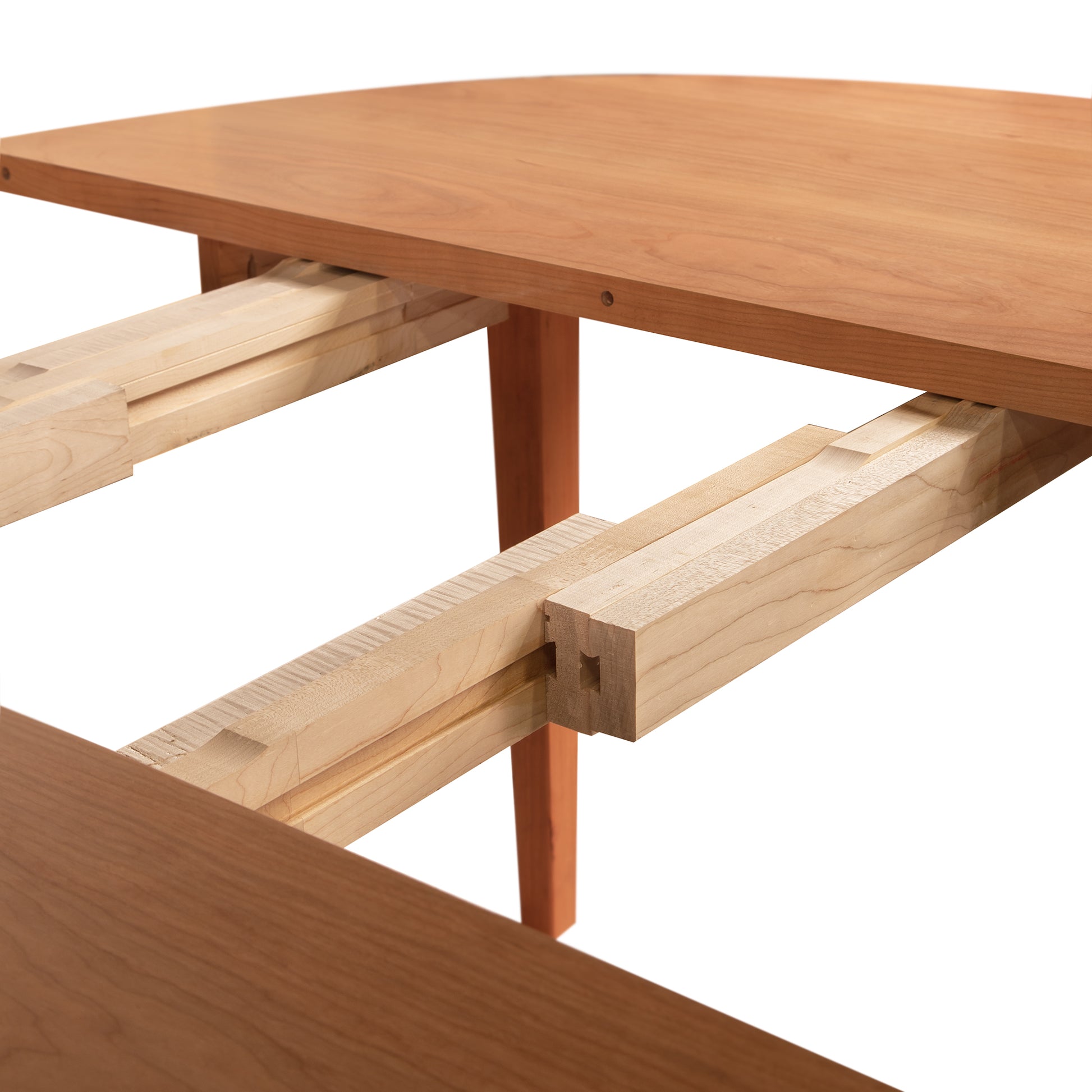 Close-up of a Maple Corner Woodworks Vermont Shaker Round Extension Table showing detailed joinery and craftsmanship, focusing on the intersection of the table legs and support beams on a white background.