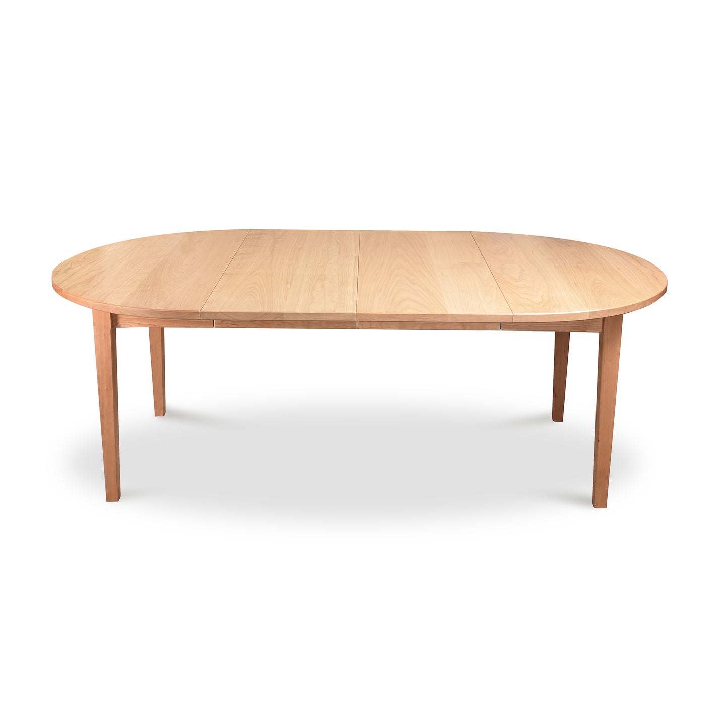 A Vermont Shaker Round Extension Table from Maple Corner Woodworks, made of natural cherry wood with an extendable center section, and standing on four slender legs, isolated against a white background.