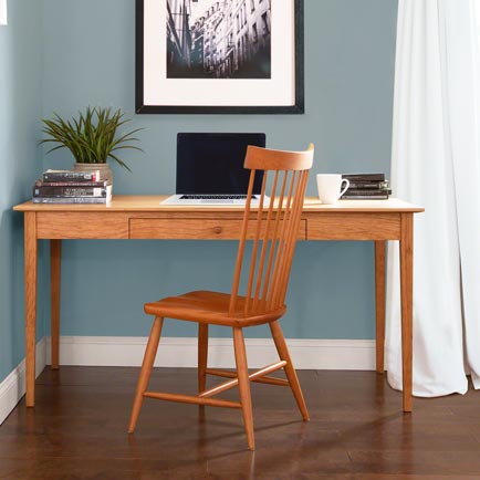 Handcrafted wooden desk and chair featuring a sleek laptop, stacked books, and a small green plant.