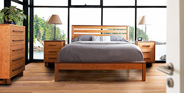 Wooden bed with gray bedding and two matching wooden dressers in a modern bedroom.