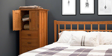 Solid wooden bed with plaid bedding and a small open-door wooden cabinet.