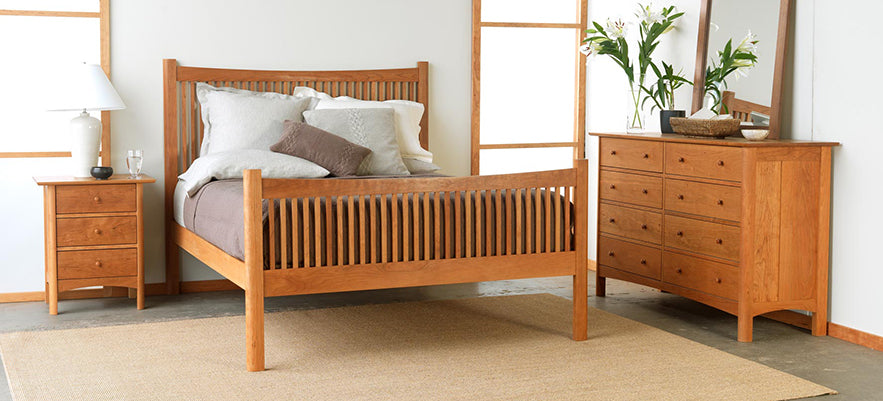 Wooden bed frame with intricate detailing, accompanied by matching bedside tables and a dresser with mirror.