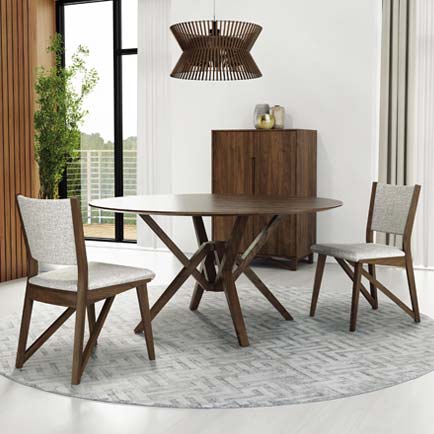 A dining area with a round wooden table and two matching wooden chairs with light gray cushions. A wooden cabinet is in the background against a white wall. The room has light-colored flooring and a large window with a partial view of greenery outside.