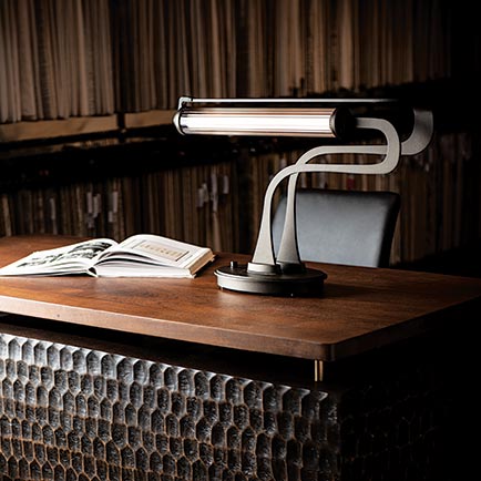 Wooden desk featuring a modern desk lamp, open book, and chair.