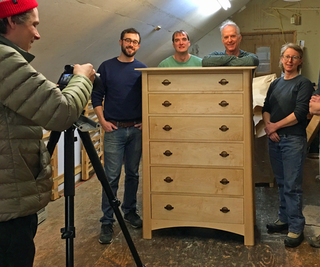 A group of people standing in front of a wooden dresser.
