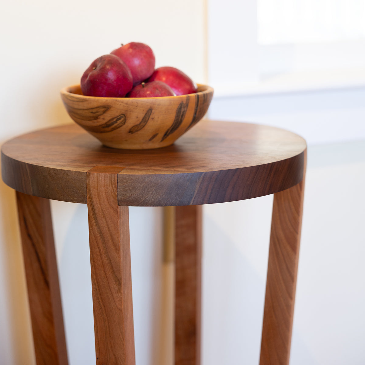 Mike Messer Cherry & Walnut Artisan End Table—floor model—with a wooden bowl of red apples displayed on its surface.