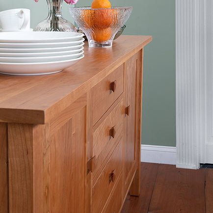 A wooden dining room table with a bowl of oranges on it.
