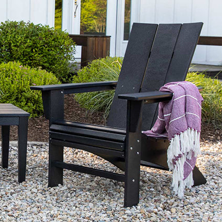 A black adirondack chair and table in a gravel yard.