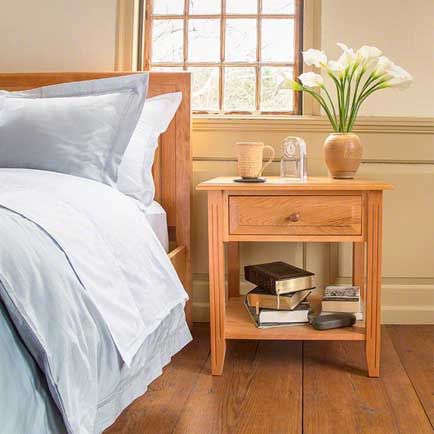 A bed with a nightstand and a vase of flowers.