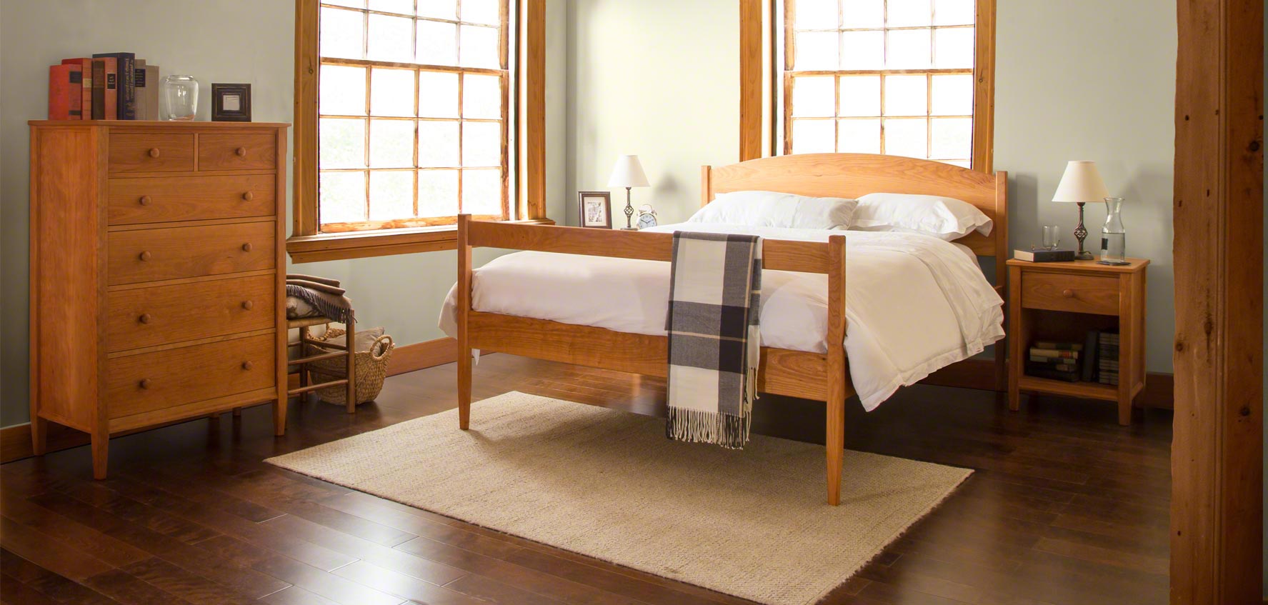 A bedroom with a bed, dresser, and two windows.