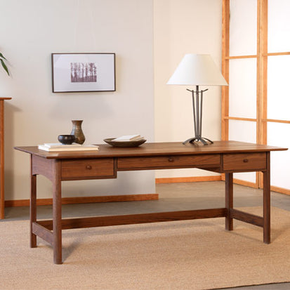 A wooden desk in a room with a lamp.