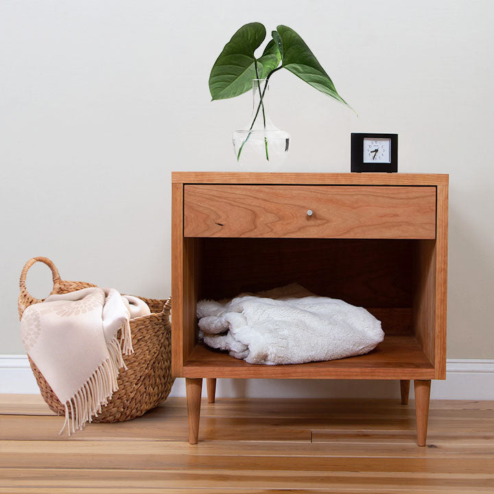A wooden nightstand with a plant and a basket.