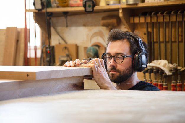 A craftsman measuring a high-quality wooden plank, showcasing fine American-made furniture craftsmanship.