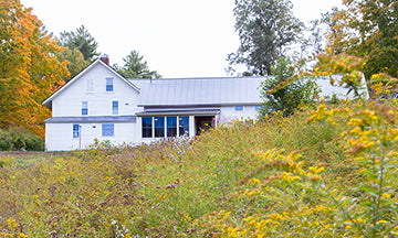 White farmhouse with metal roof in a serene natural setting.