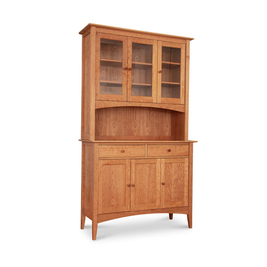 The American Shaker 50" China Cabinet by Maple Corner Woodworks is crafted from solid wood, showcasing American craftsmanship with a two-door glass display top, dual drawers, and a two-door bottom storage. Featuring a natural finish that highlights Vermont-made quality furniture, this elegant piece is perfect for those seeking shaker style furniture with slightly tapered legs for added elegance.