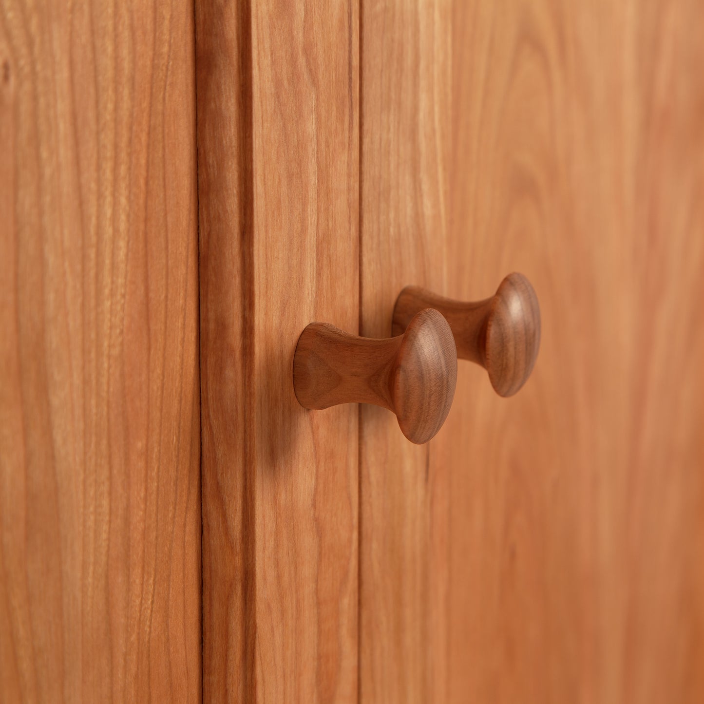 Close-up of an American Shaker Medium Sideboard by Maple Corner Woodworks, featuring two knob handles and solid hardwood construction. The cabinet showcases a natural wood grain texture with a light brown finish, highlighting exquisite Vermont craftsmanship.