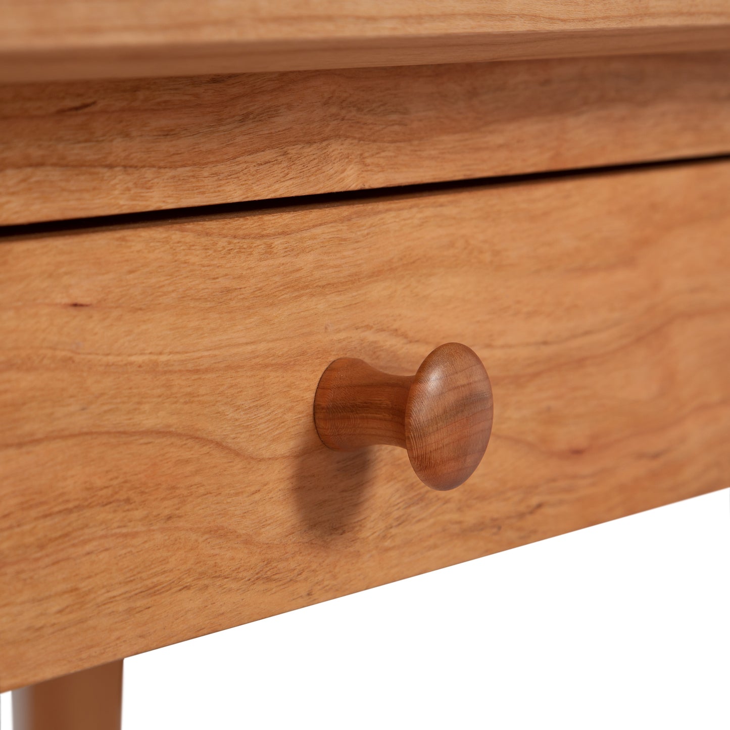 Close-up of a wooden drawer with a matching round wooden knob, crafted from natural cherry hardwood. The wood shows a light brown grain pattern. The front edge of the drawer is visible, with no other parts of the American Shaker Writing Desk - 24"x54" - Floor Model by Maple Corner Woodworks in the frame—an exquisite piece by Vermont craftsmen.