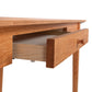 A Maple Corner Woodworks American Shaker writing desk with an open drawer, showcasing its handle and the grain of the sustainably harvested hardwood.