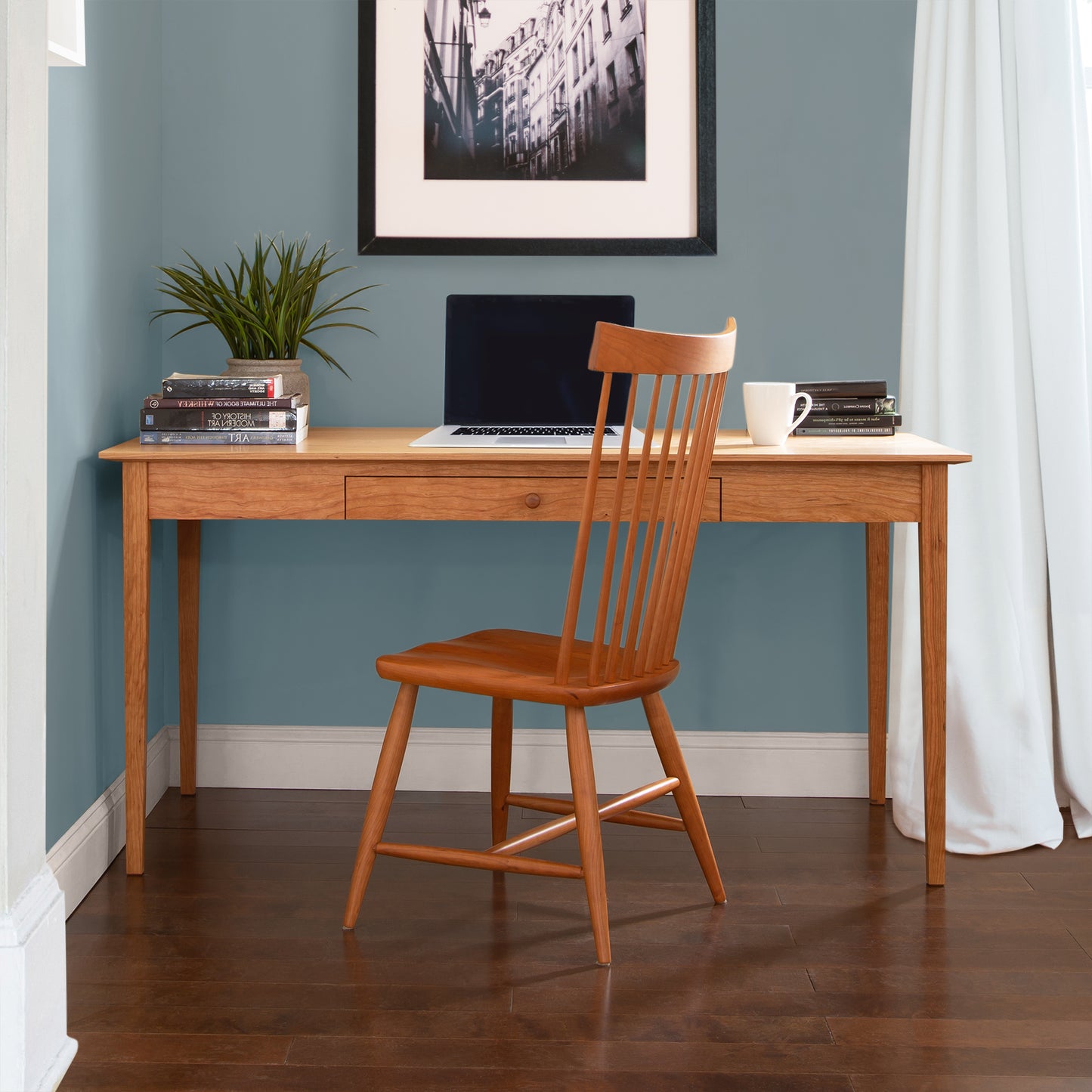 A Maple Corner Woodworks American Shaker Writing Desk and chair made of sustainable hardwood in a room with blue walls.