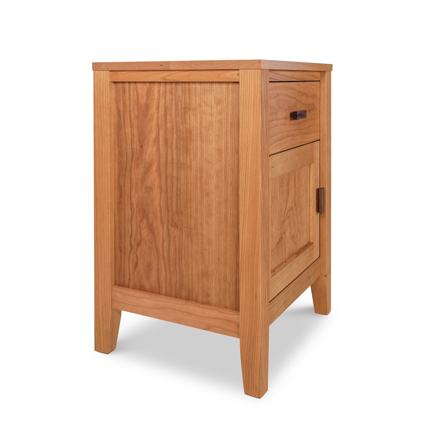 An Andover Modern 1-Drawer Nightstand with Door crafted by Maple Corner Woodworks, featuring a single door and an upper drawer made from sustainable hardwoods. It stands on angled legs, employs a light brown hue, and showcases