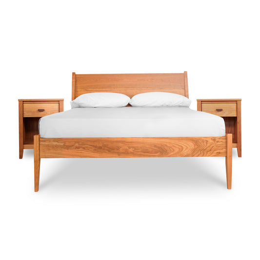 The Maple Corner Woodworks Andover Modern 3-Piece Bedroom Set - Ready to Ship features a solid wood incline bed with a striking wooden headboard. Showcased in the image, the bed includes a white mattress and two white pillows. Complementing the mid-century modern design are matching wooden bedside tables, each equipped with a single drawer and an additional shelf beneath.