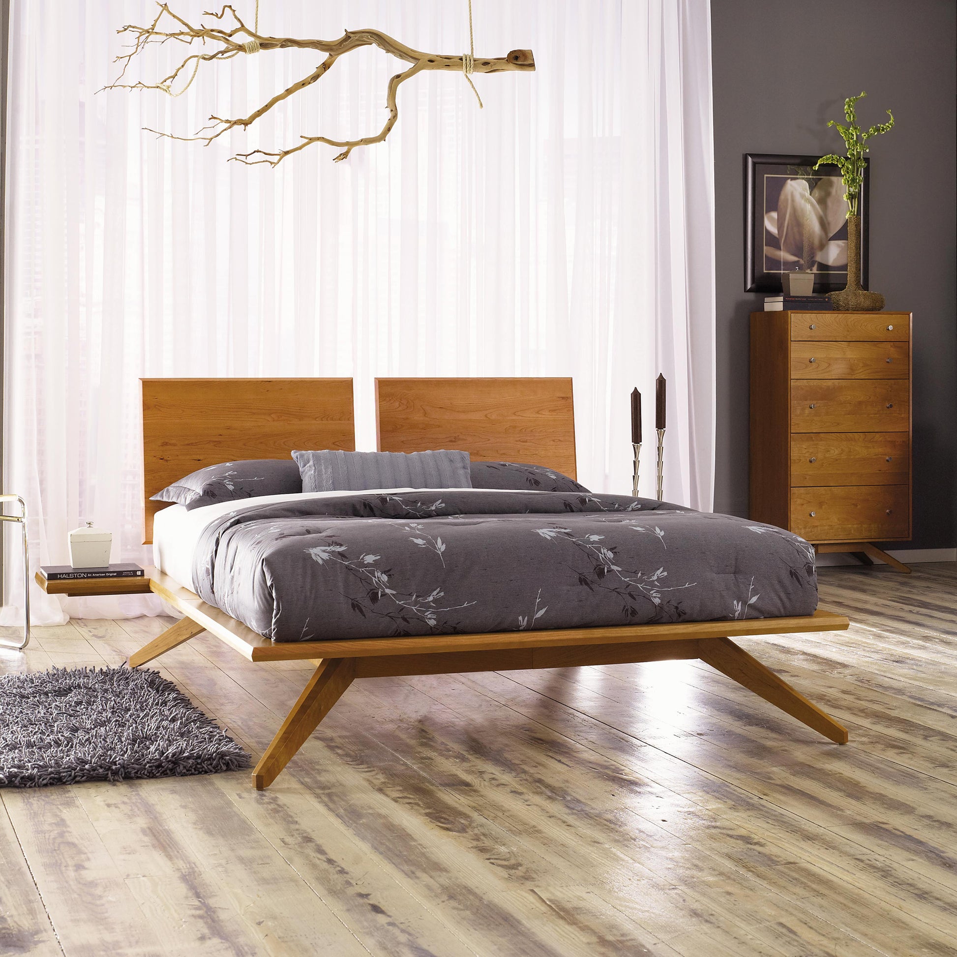 Astrid Platform Bed by Copeland Furniture in a modern setting with gray bedding, complemented by a tall dresser and a rug, on light wood flooring.