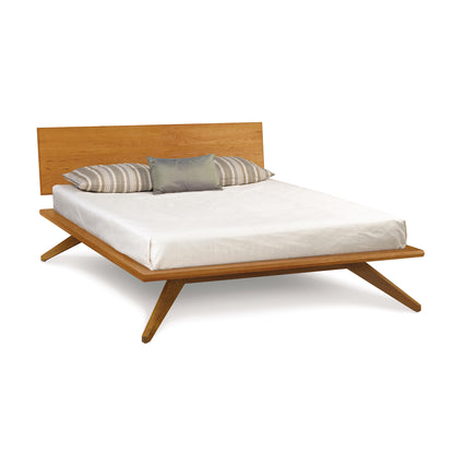 A modern eco-friendly Astrid Cherry Platform Bed with a simple headboard, featuring a white mattress and a set of striped and solid-colored pillows. (Brand Name: Copeland Furniture)