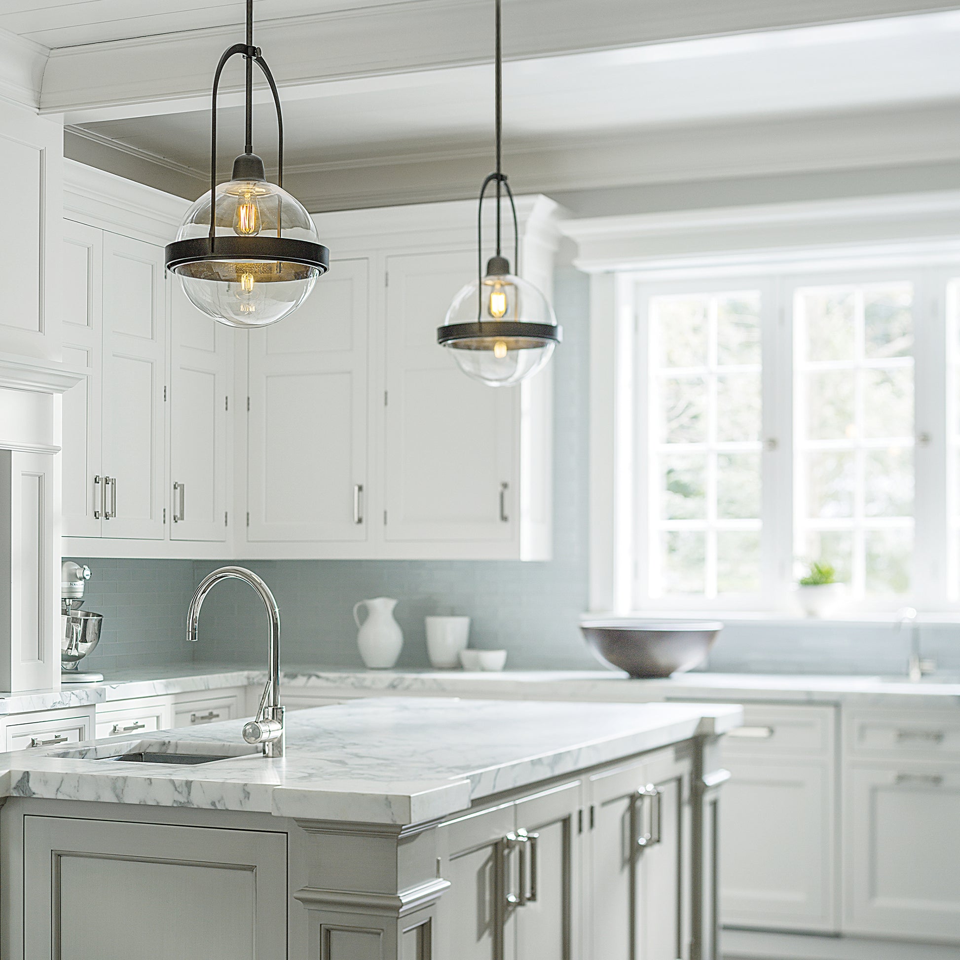 A kitchen with white cabinets illuminated by a handcrafted Hubbardton Forge Atlas Mini Pendant light.
