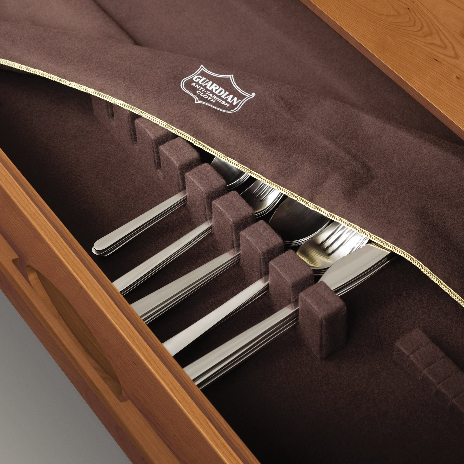A set of silver cutlery neatly placed in a wooden Copeland Furniture storage case, lined with protective brown fabric.