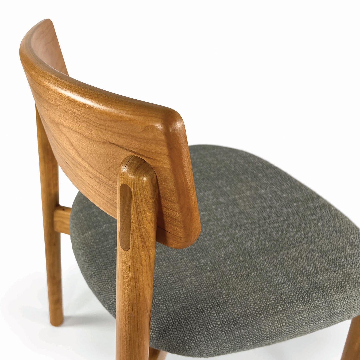 Baton Chair by Copeland Furniture with a sculpted curved backrest and plush gray seat, expertly crafted in solid wood, shown from the rear view.