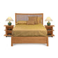 A neatly made Copeland Furniture Berkeley Cherry Storage Bed in the American Craftsman style with a gold-colored comforter and matching pillows flanked by two bedside tables with table lamps and small decorative items.
