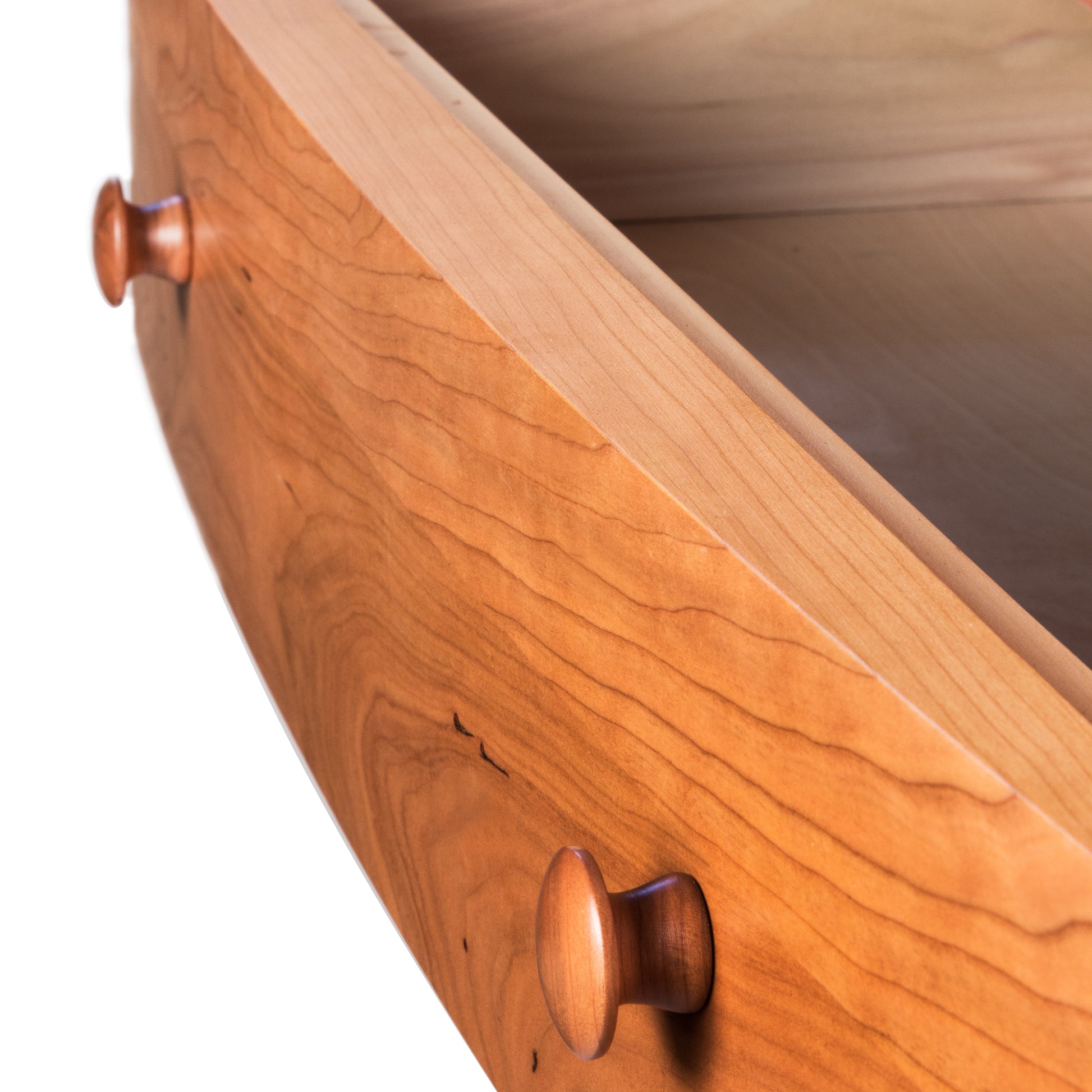 Close-up of the corner of an open wooden drawer from the Bow Front 5-Drawer Chest by Lyndon Furniture, showcasing American-made craftsmanship. Features two round wooden knobs and smooth light-brown cherry wood grain. The empty drawer highlights its solid wood construction and high-quality finish, ideal for customers seeking Vermont made furniture.