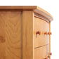 Close-up of a Lyndon Furniture Bow Front 6-Drawer Dresser, handmade in Vermont. The image highlights the dresser's corner and front with a light wood finish, rounded edges, and small wooden knobs on its drawers. Visible wood grain on the side panel emphasizes the high quality solid wood craftsmanship of this American made furniture piece.