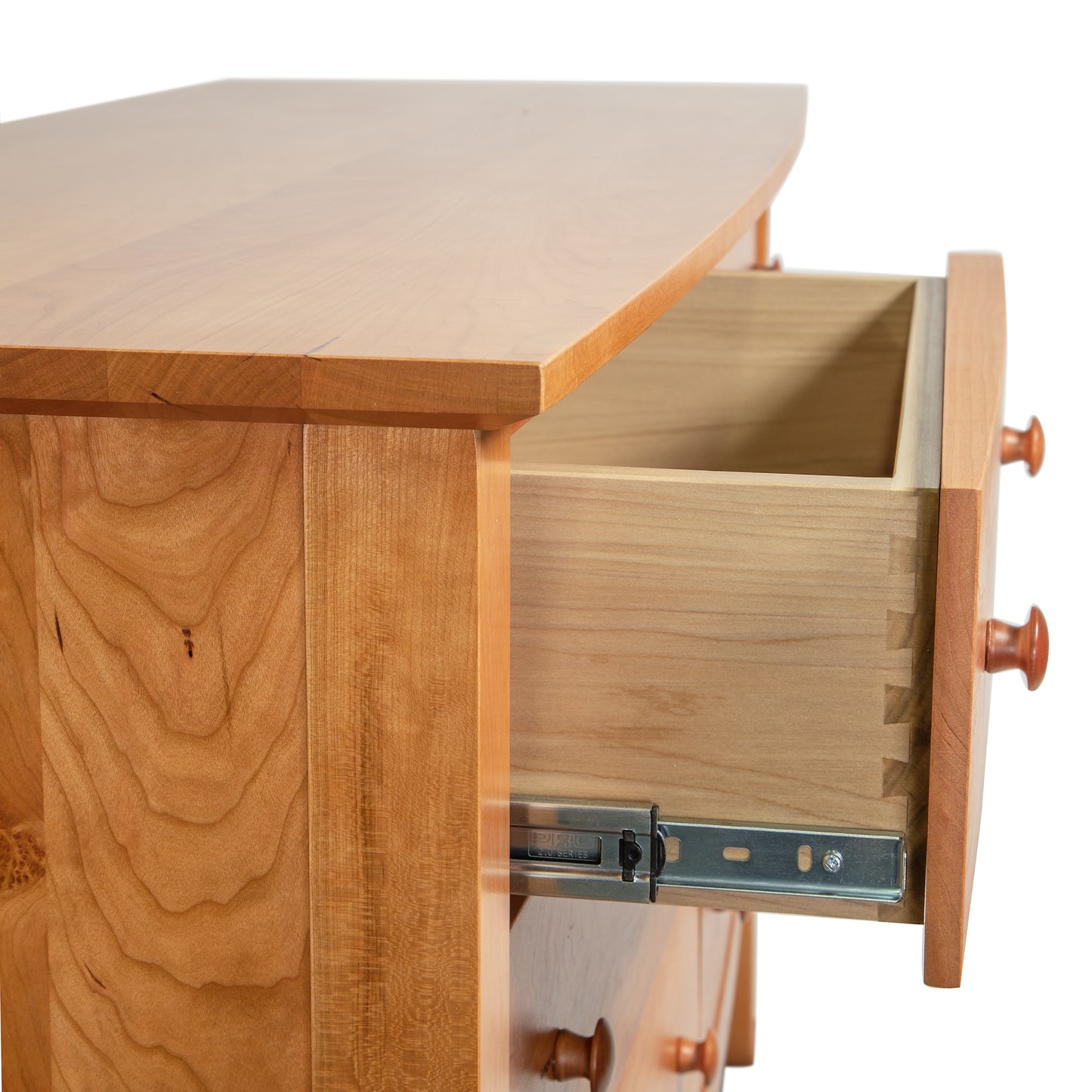 Close-up of a solid wood double dresser with an open drawer featuring dovetail joints and metal slides. The Bow Front 6-Drawer Dresser by Lyndon Furniture, handmade in Vermont, showcases American craftsmanship with its smooth light-toned finish and round wooden knobs. Ideal for those seeking cherry wood furniture or American made bedroom furniture.