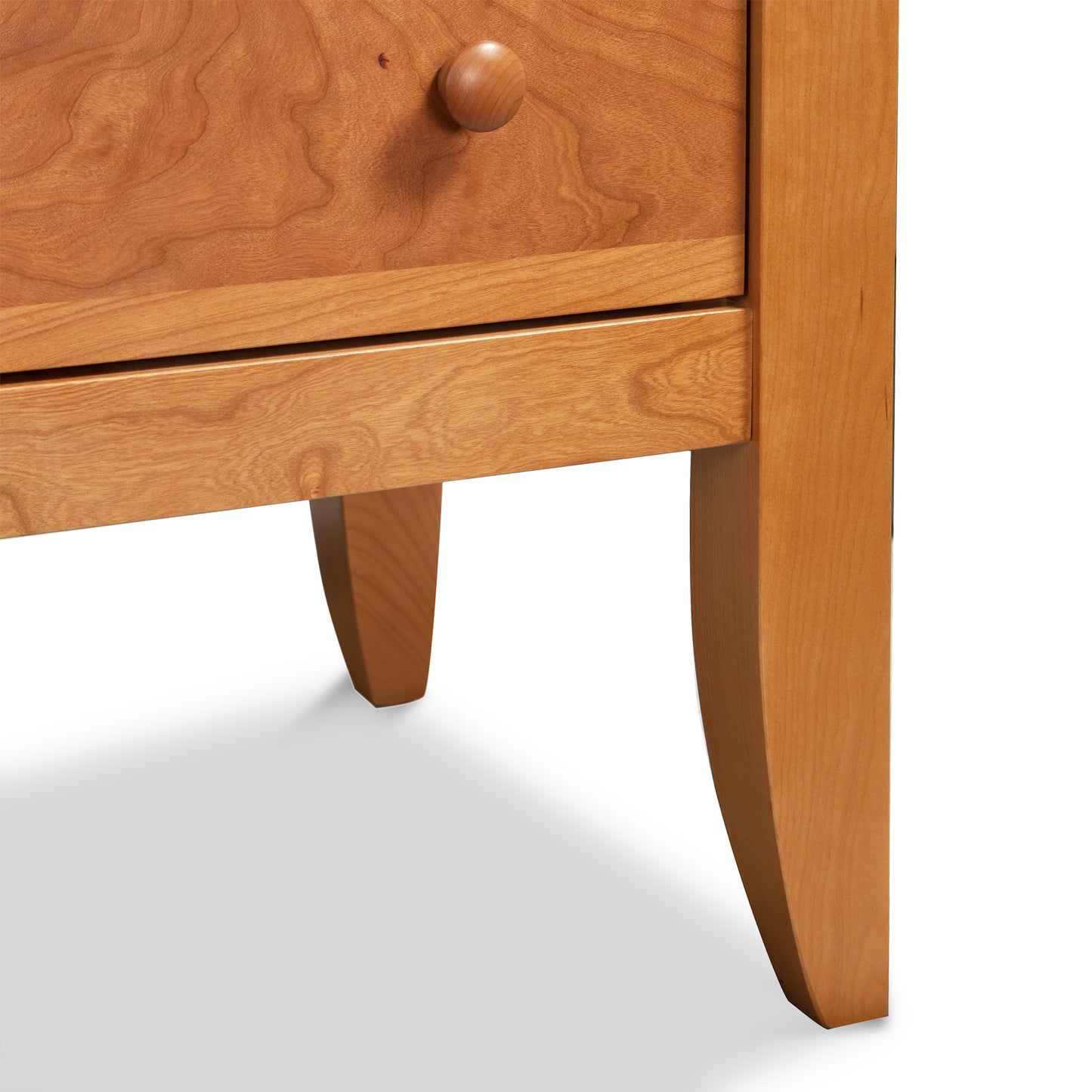 Close-up of Lyndon Furniture's Bow Front 6-Drawer Dresser showcasing Vermont-made craftsmanship. The image highlights a drawer with a round wooden knob, tapered legs, and a natural wood grain finish. Ideal for solid wood furniture enthusiasts and those searching for handmade American furniture. Plain white background emphasizes the dresser's fine details.