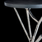 Introducing the Brindille Wood Top Accent Table by Hubbardton Forge, which showcases a meticulously handcrafted design. It features a smooth, dark Vermont Maple top, complemented by intricately angular metal legs with a twisted appearance and a shiny finish set against a sleek black backdrop.