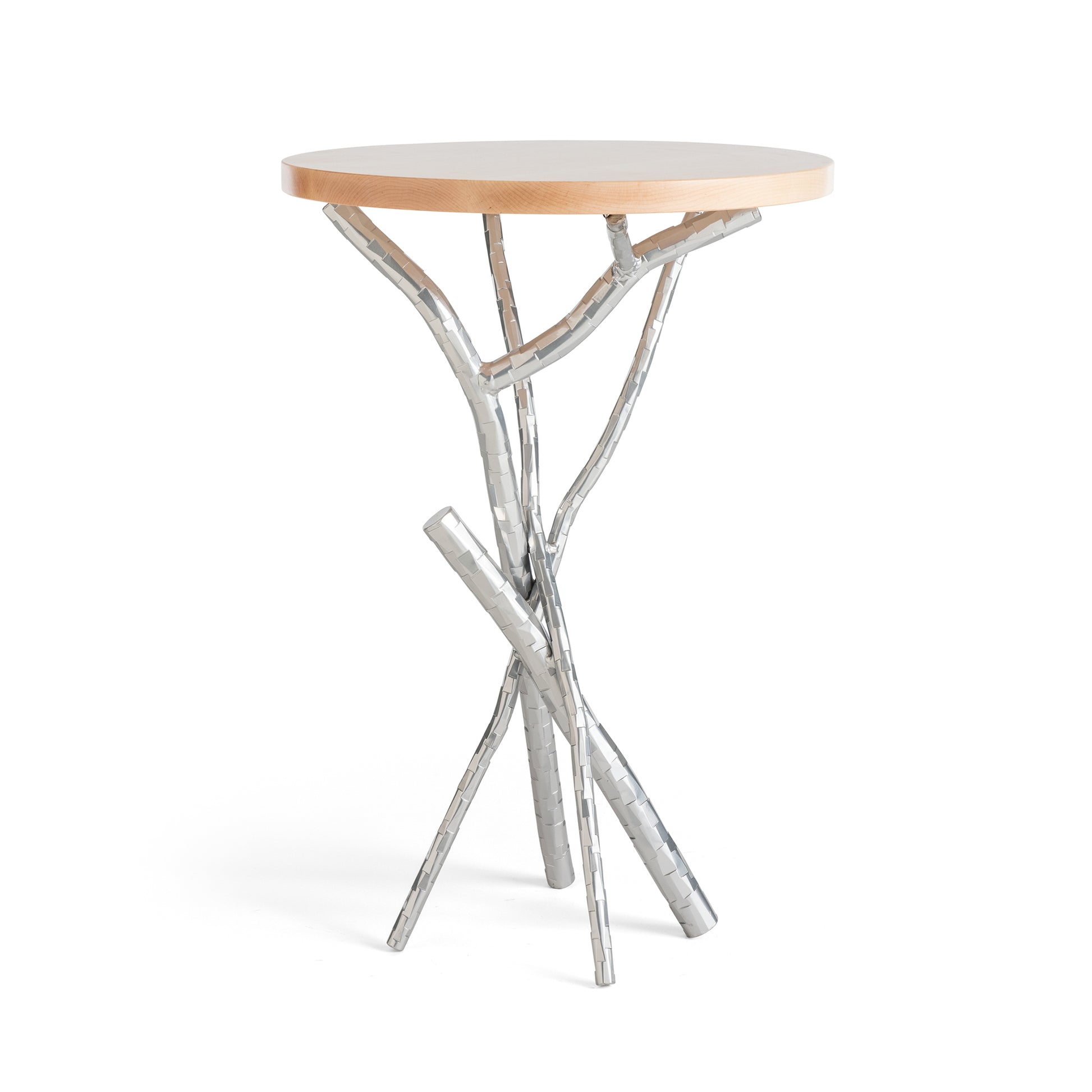 The Brindille Wood Top Accent Table by Hubbardton Forge features a Vermont maple top paired with a distinctive metal base crafted to resemble intertwined branches. The handcrafted metal boasts a silver finish, offering a contemporary yet natural aesthetic, and the table is elegantly displayed against a white background.