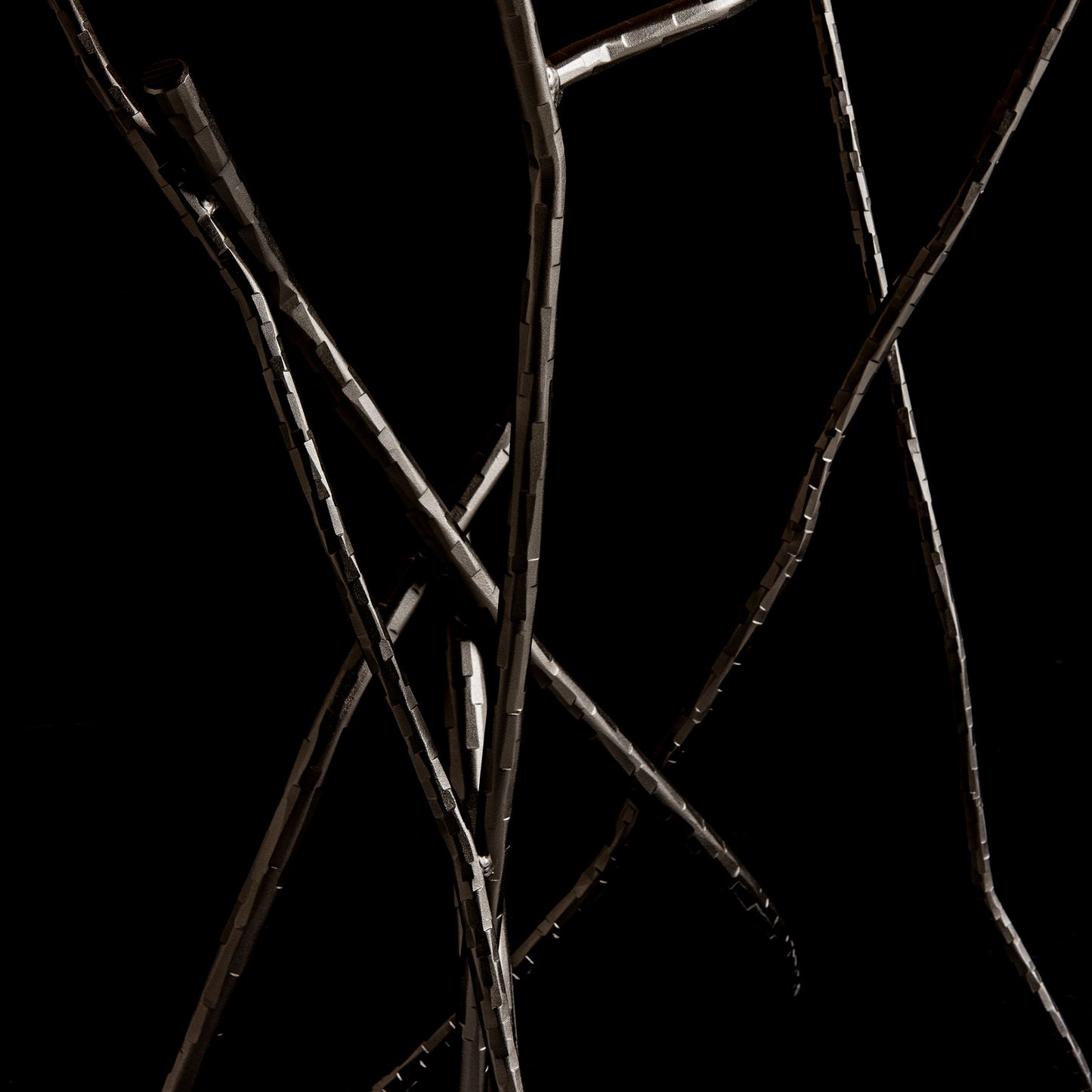 A close-up of several intertwined, slender metal rods against a black background, reminiscent of an abstract design by Hubbardton Forge. The textured surface and varying angles evoke motion and complexity, similar to the artistic flair seen in the Brindille Wood Top Console Table.