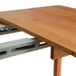 A wooden dining room furniture piece, known as the Vermont Furniture Designs Burlington Shaker Extension Dining Table, with an extended metal sliding mechanism visible, showing the table's extendable feature.