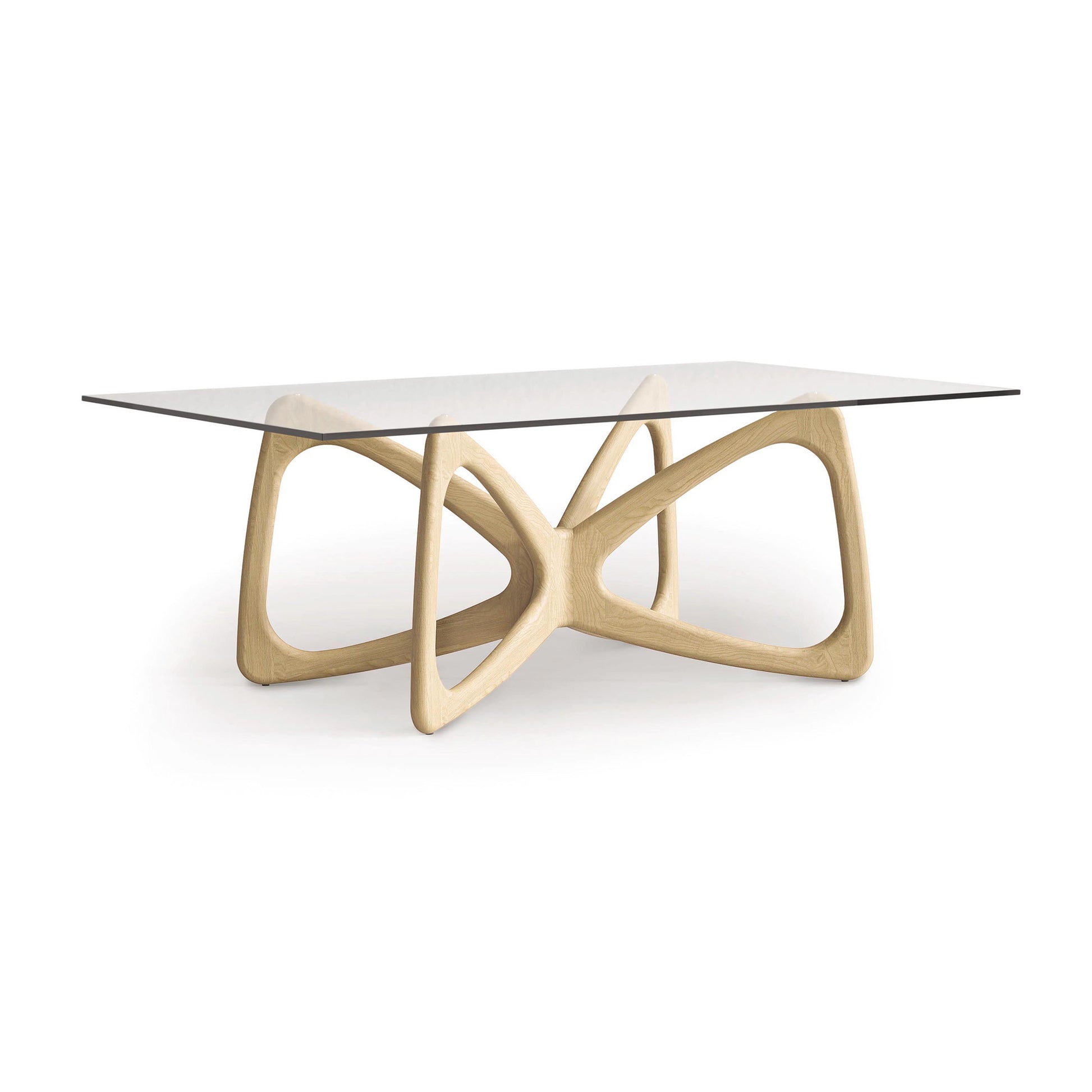 The Butterfly Glass Top Dining Table by Copeland Furniture showcases a modern design with a rectangular glass top and an intricately curved base made from sustainably sourced hardwoods. The light-colored wood provides a striking contrast to the sleek glass surface, creating an elegant centerpiece for any room.