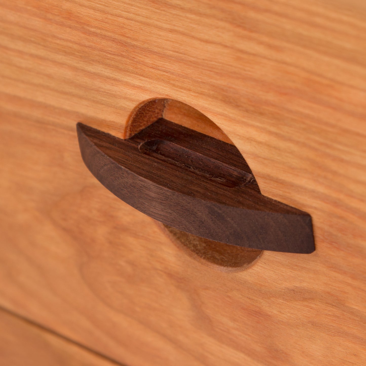 Close-up of an elongated oval dark wood handle on a Cherry Moon 3-Drawer Nightstand by Maple Corner Woodworks, displaying American-made, handcrafted Vermont solid cherry wood furniture.