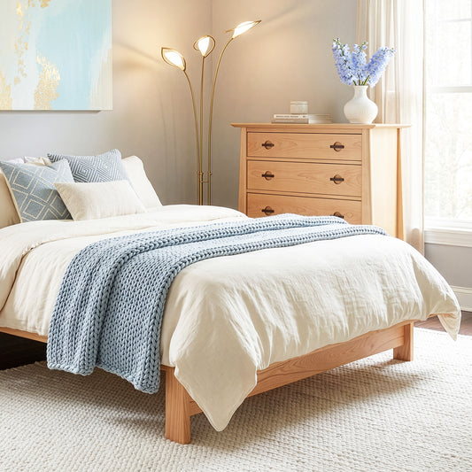 Maple Corner Woodworks Cherry Moon 4-Drawer Chest next to a neatly made bed with blue and white bedding, showcasing fine American craftsmanship.