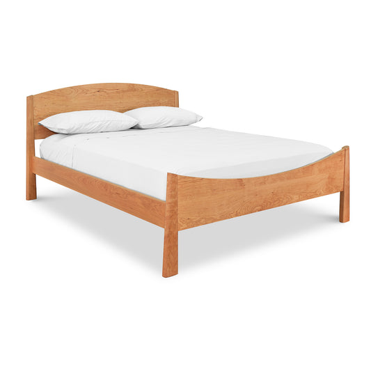 A simple solid wood Cherry Moon Bed frame from Maple Corner Woodworks, featuring a clean-lined headboard and footboard. The bed is made up with white bedding, including a fitted sheet, flat sheet, and two.