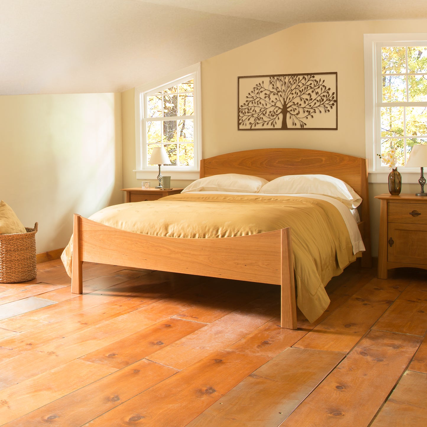 A bedroom with a wooden floor and the Maple Corner Woodworks' Cherry Moon Bed featuring beige bedding. Two windows above the headboard let in natural light, accentuating the tree artwork on the wall. Handmade solid wood nightstands sit on either side, enhancing the eco-friendly charm of this serene space.