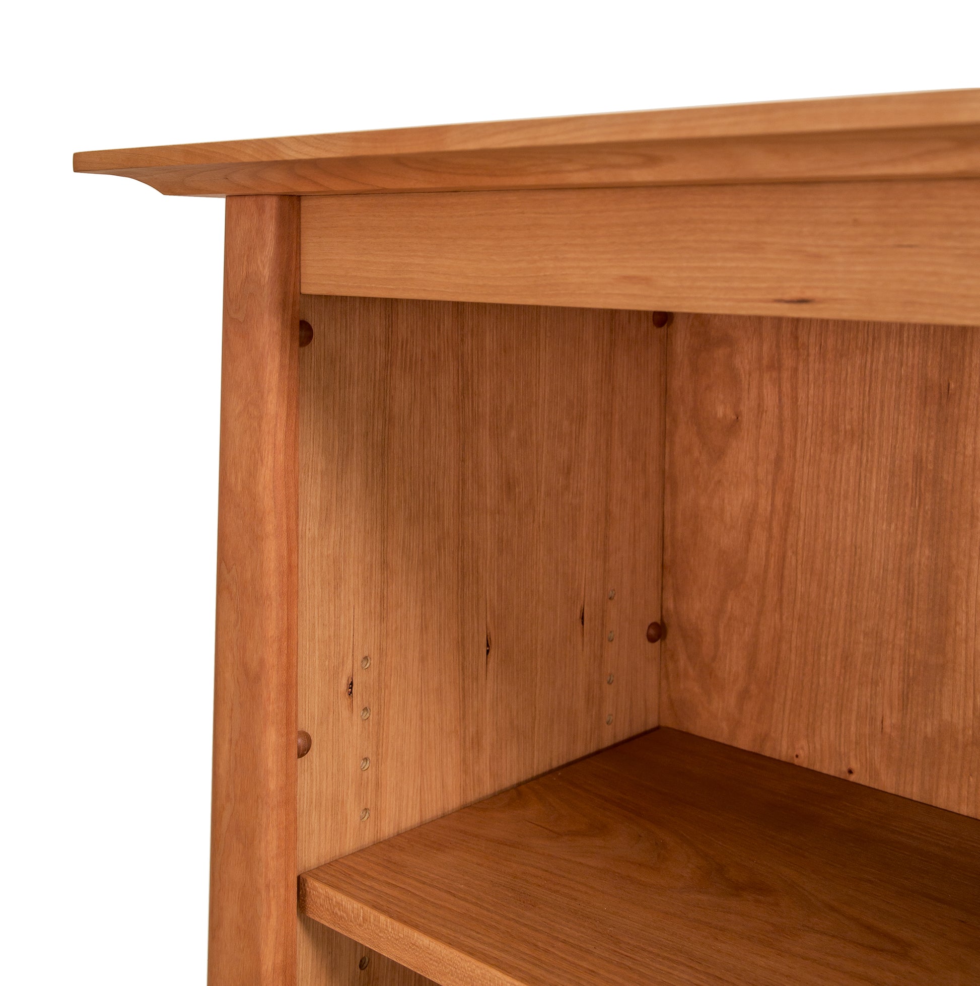 Close-up of a Cherry Moon Bookcase corner from Maple Corner Woodworks, crafted from sustainably harvested hardwoods, showing the tabletop, a shelf, and the end panel with visible wood grain and fastening hardware holes.