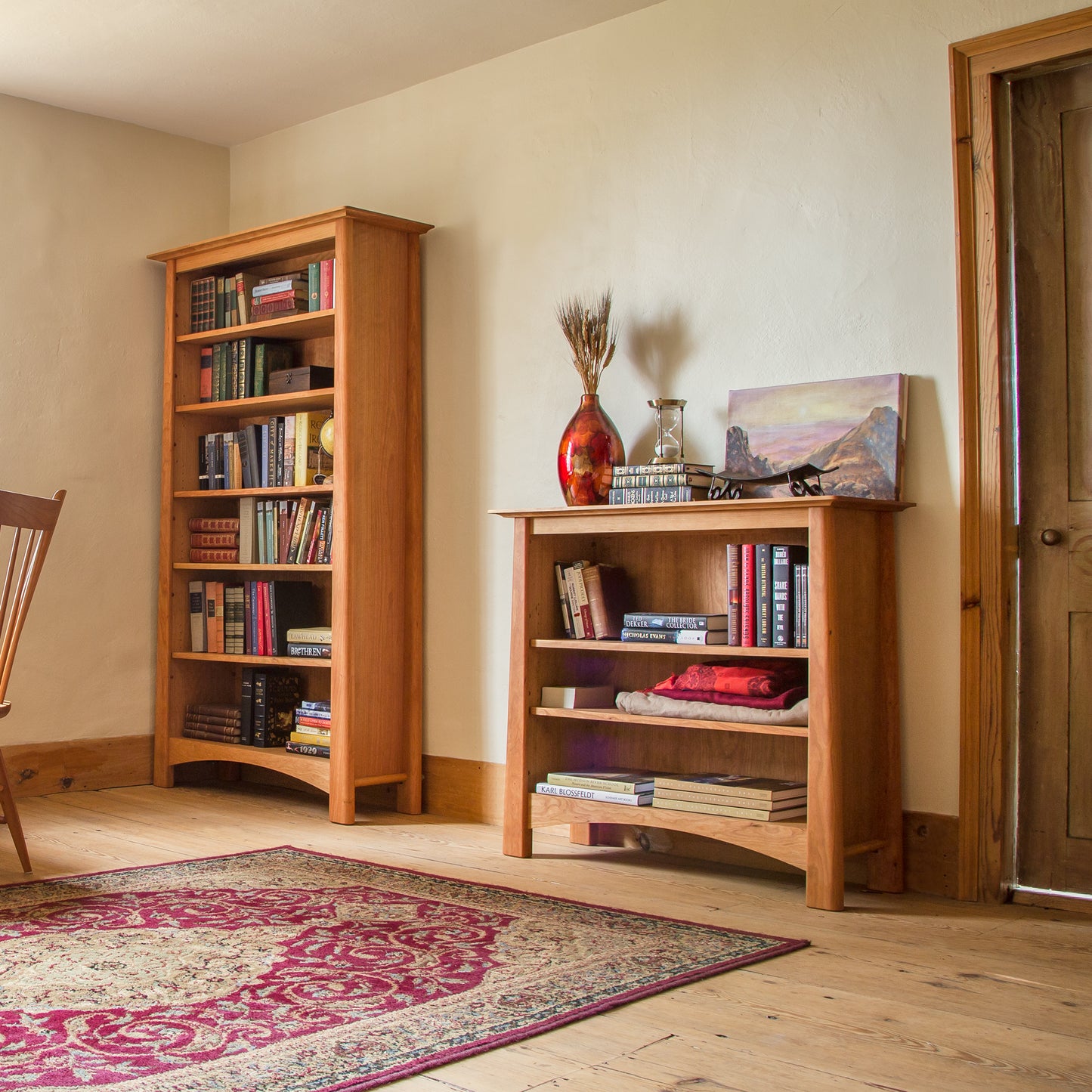 Cherry Moon Bookcases from Maple Corner Woodworks beside a wooden chair, showcasing the elegance of fine craftsmanship and beautiful cherry wood grain.