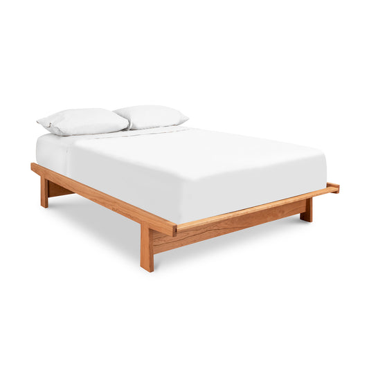 This image showcases a Cherry Moon Dovetail Platform Bed by Maple Corner Woodworks, crafted from sustainably harvested cherry wood. The bed features an eco-friendly oil finish and low, sturdy legs, presenting a simple, minimalist design. Neatly made with white bedding and pillows, this American-made bed embodies modern and clean aesthetics in solid wood furniture craftsmanship.