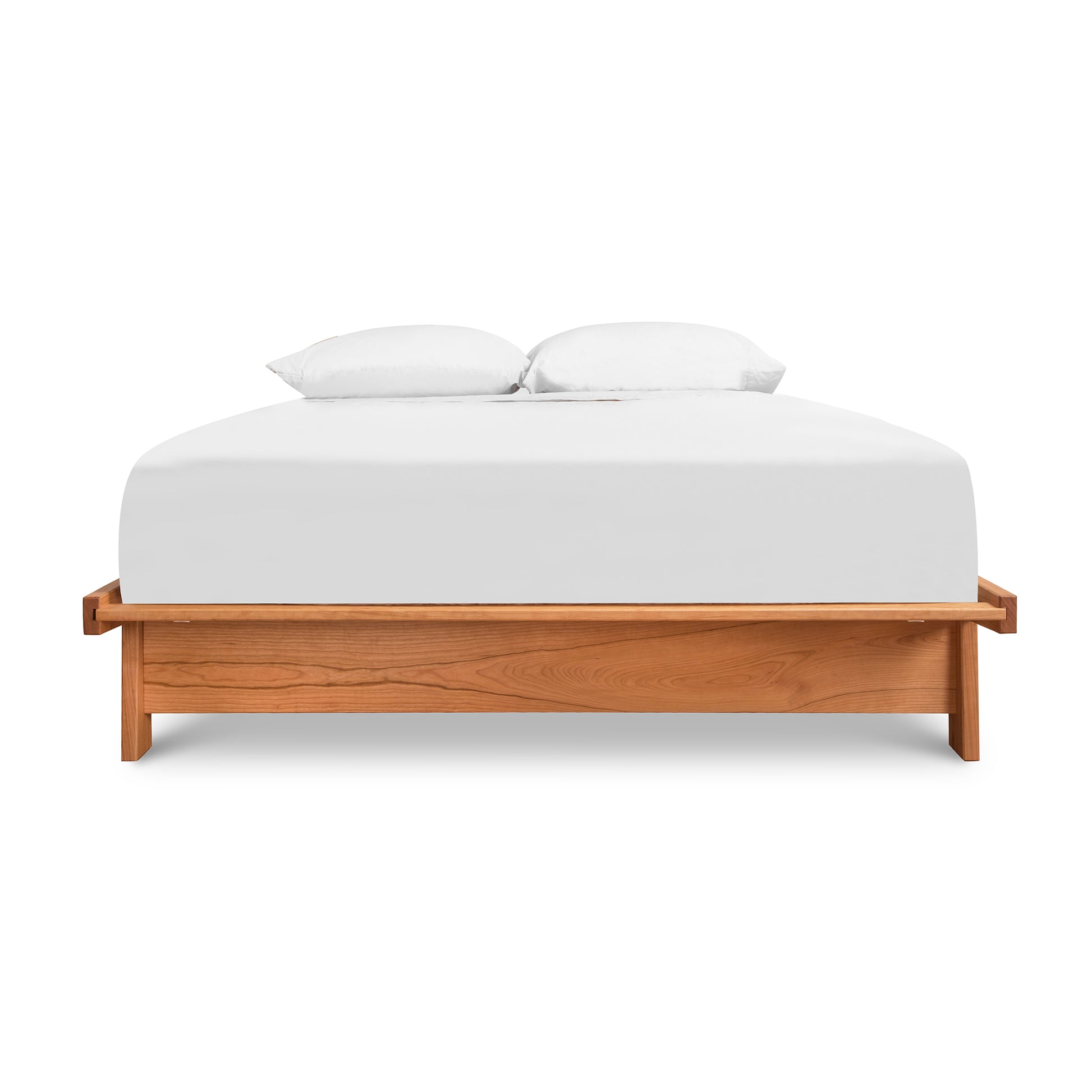 A minimalist Maple Corner Woodworks Cherry Moon Dovetail Platform Bed frame made from solid sustainably harvested woods, with a white mattress and two pillows, isolated on a white background.