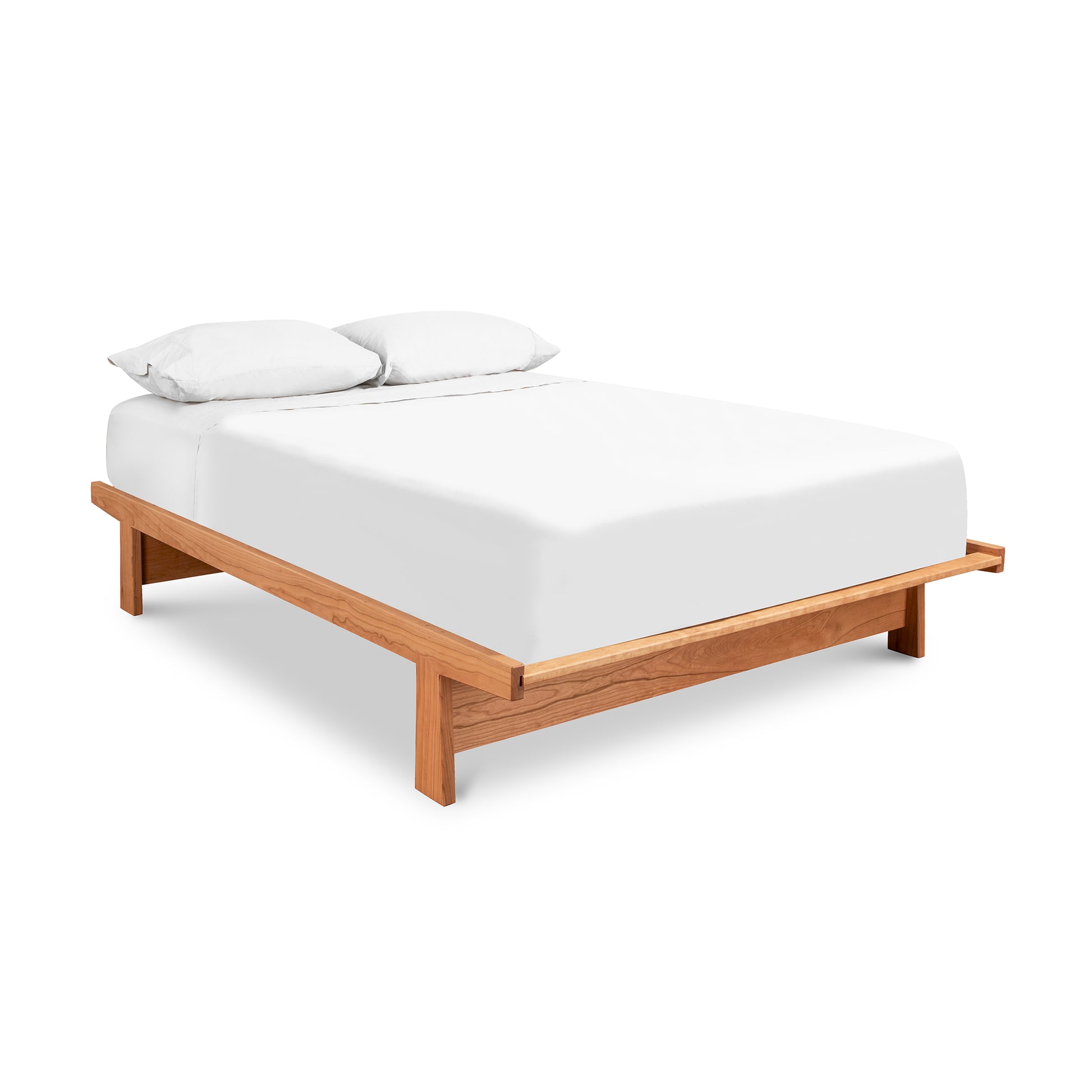 A Cherry Moon Dovetail Platform Bed from Maple Corner Woodworks, featuring a white mattress and two pillows. The frame and legs, crafted from solid sustainably harvested woods, appear to be made of light-colored wood with an eco-friendly oil.